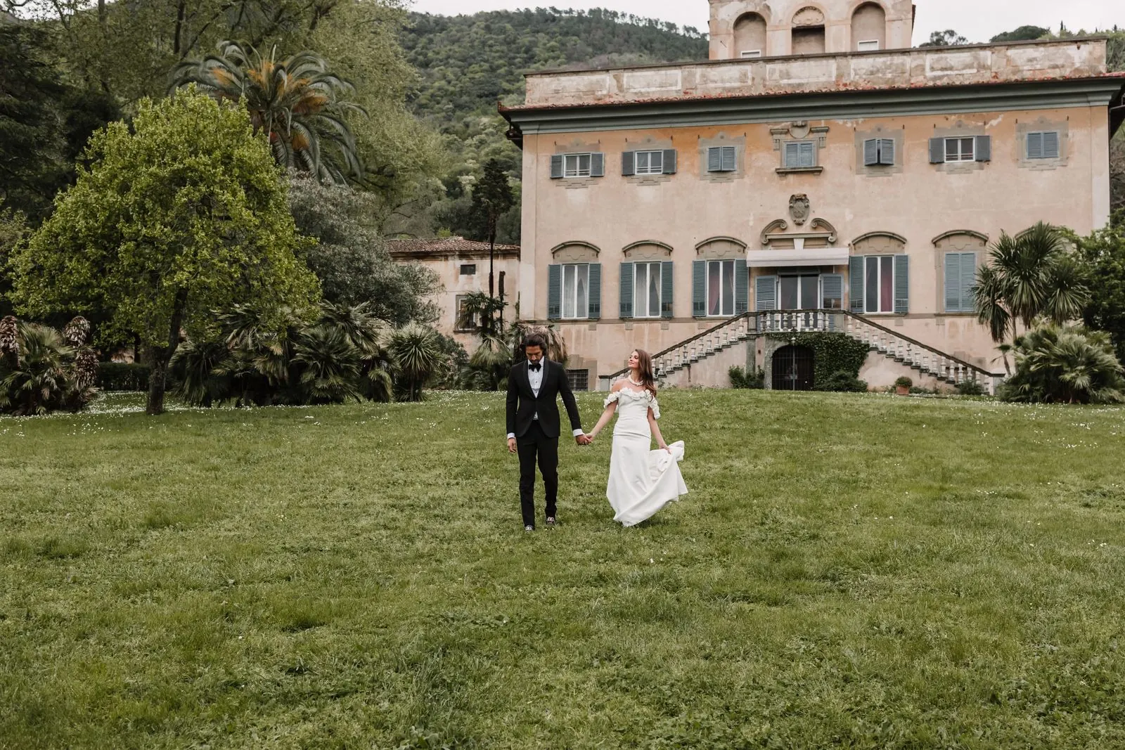 Het bruidspaar wandelt over het gazon voor Villa e Parco di Corliano in Toscane