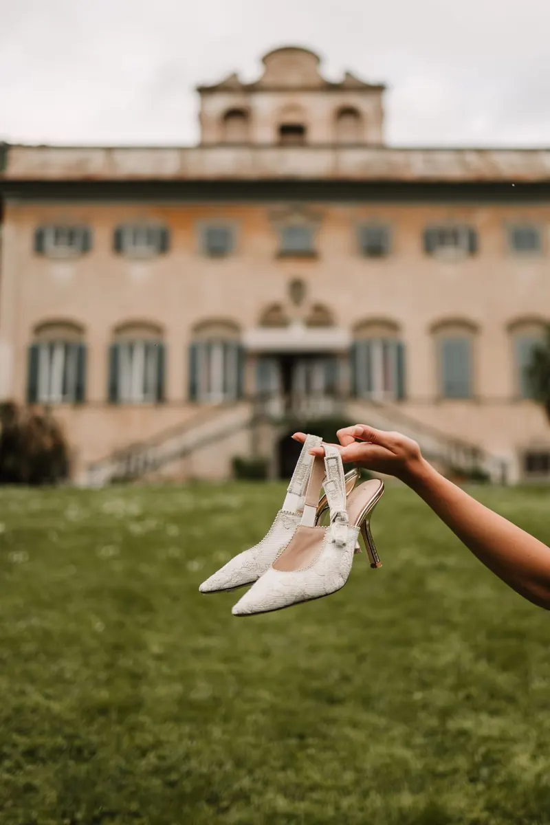 Bruidsschoenen in de hand met de villa op de achtergrond