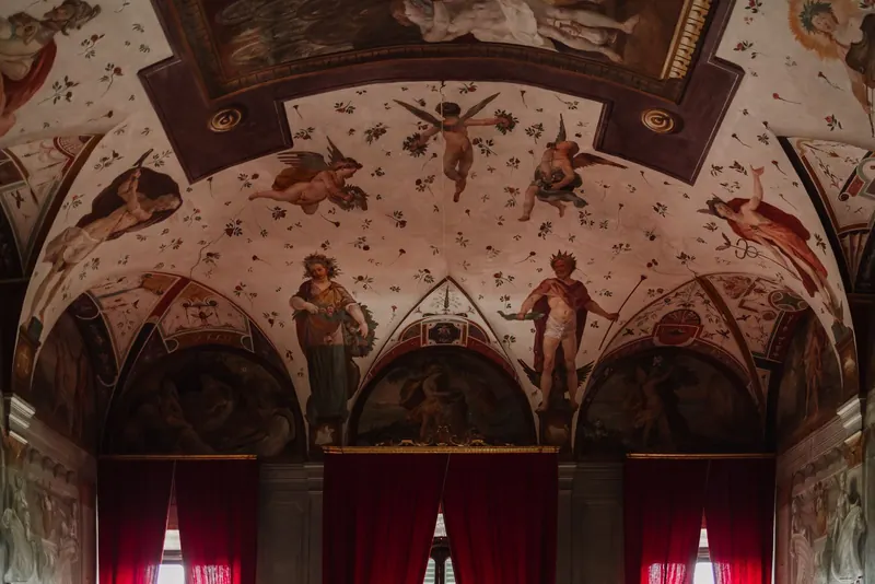 Gewelfde zaal met fresco's en rode gordijnen in Villa di Corliano