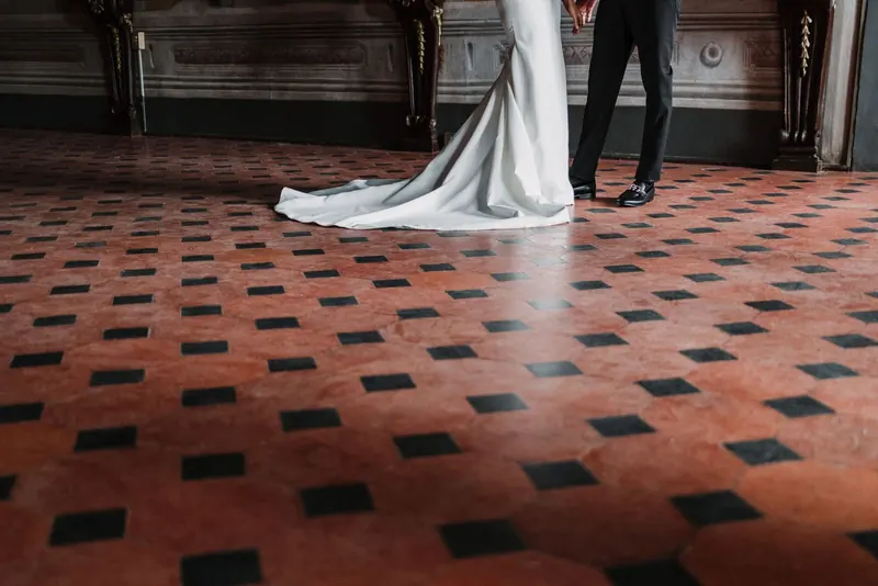 De sleep van de jurk en de schoenen van de bruidegom op de geblokte vloer