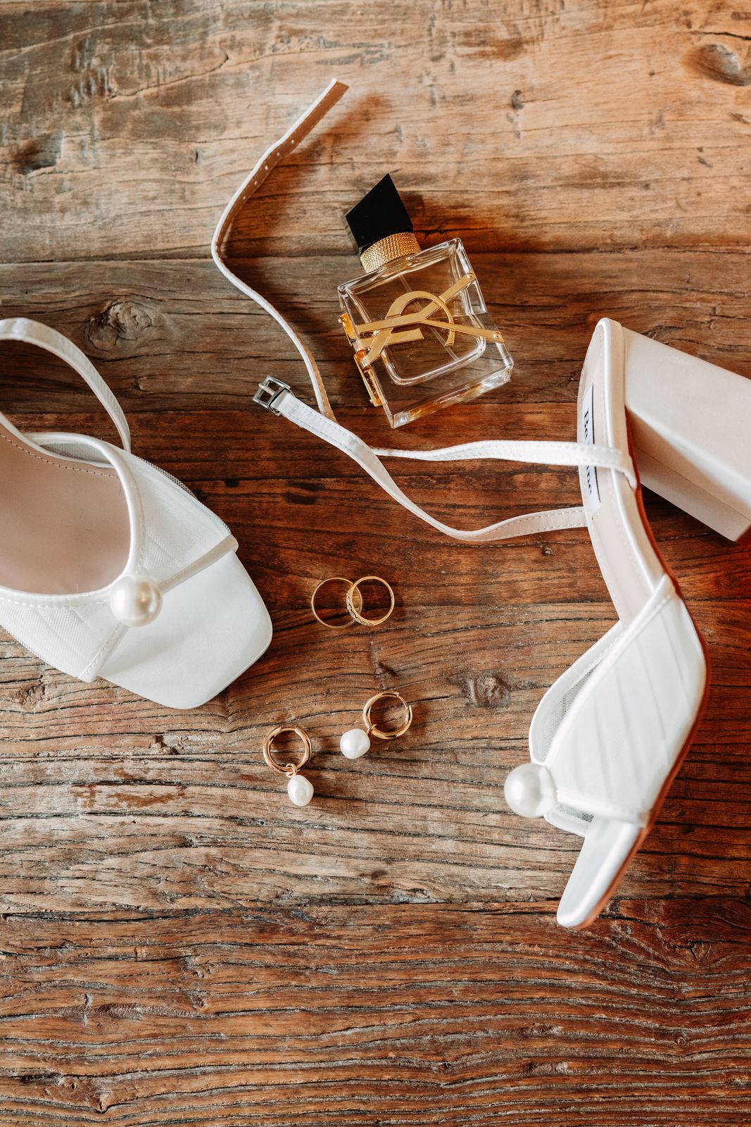 Bruidsschoenen, parfum en trouwringen op een oude houten tafel tijdens de getting ready
