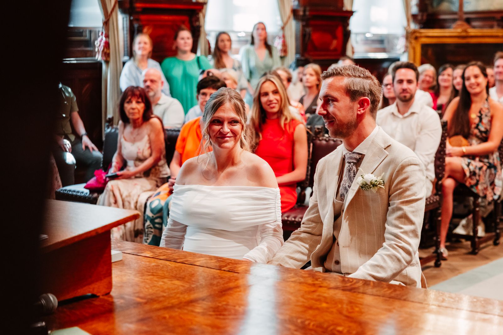 Julie en Olivier lachen tijdens de trouwceremonie met familie achter hen