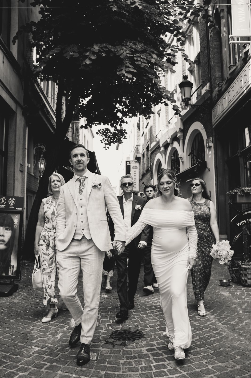 Bruidspaar en gasten wandelen door de straten van Antwerpen, monochrome foto